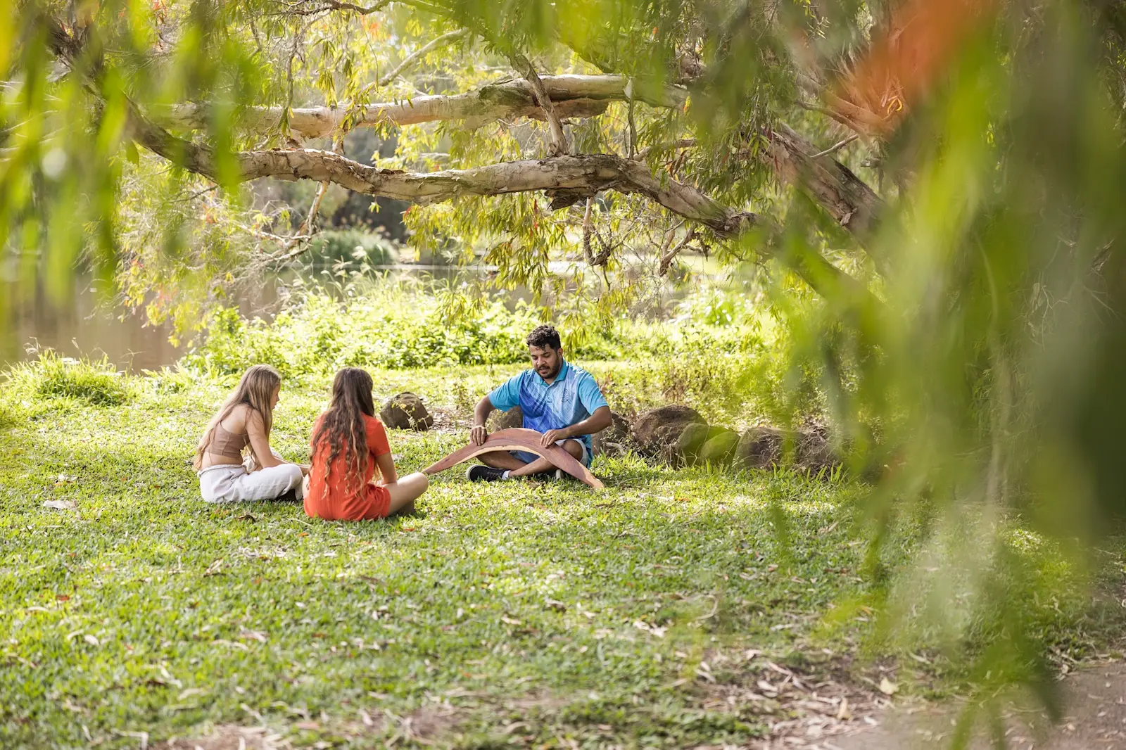Guide from Taribelang Bunda Cultural Tours sitting under a tree with guests and describing cultural tools and their uses, Bundaberg, Queensland © Taribelang Bunda Cultural Tours
